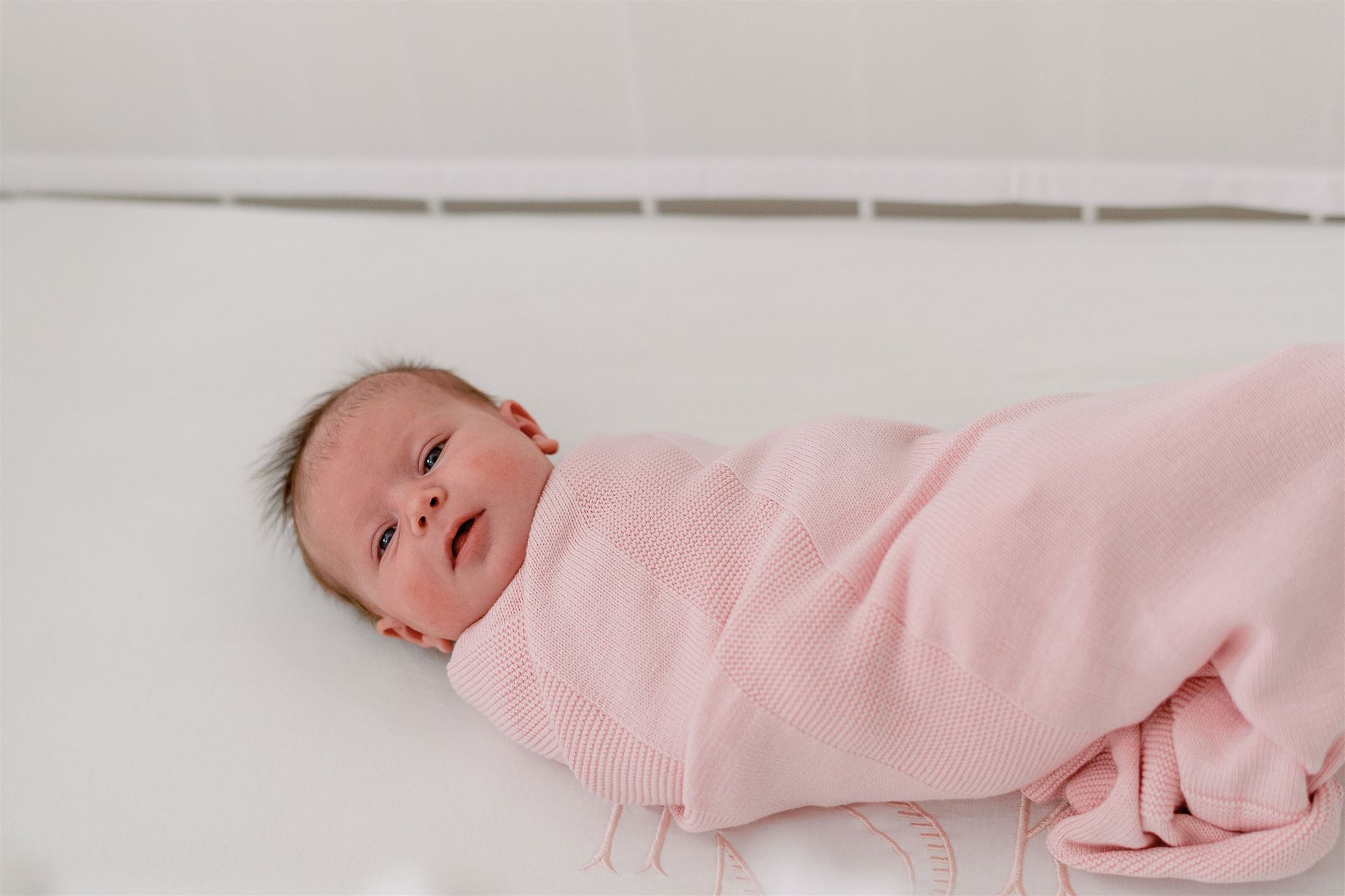 by girl swaddled in a pink blanket laying on her back in her crib