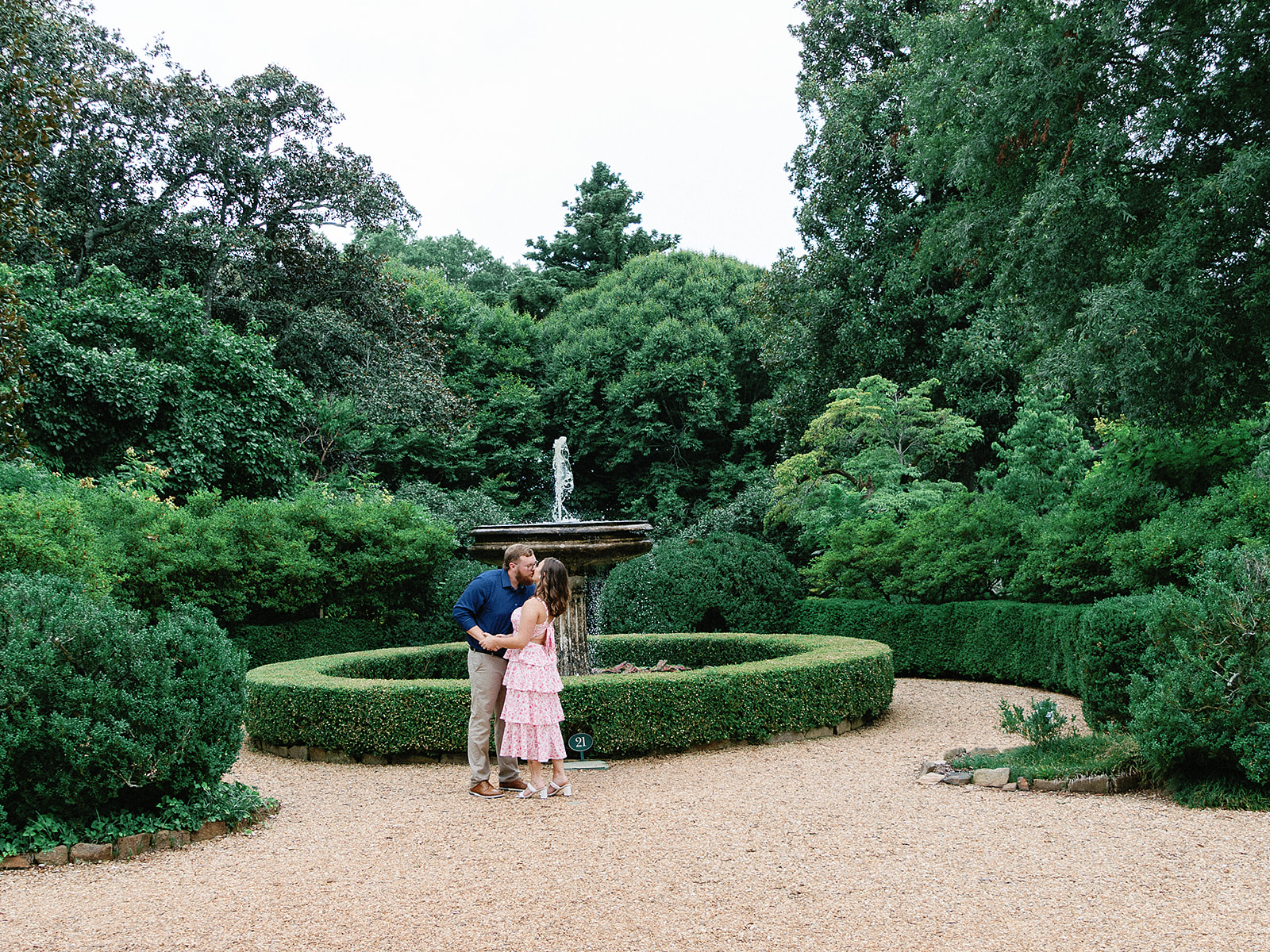 A couple, male and female kissing outside in a beautiful garden near a fountain at the hills and dales estate.