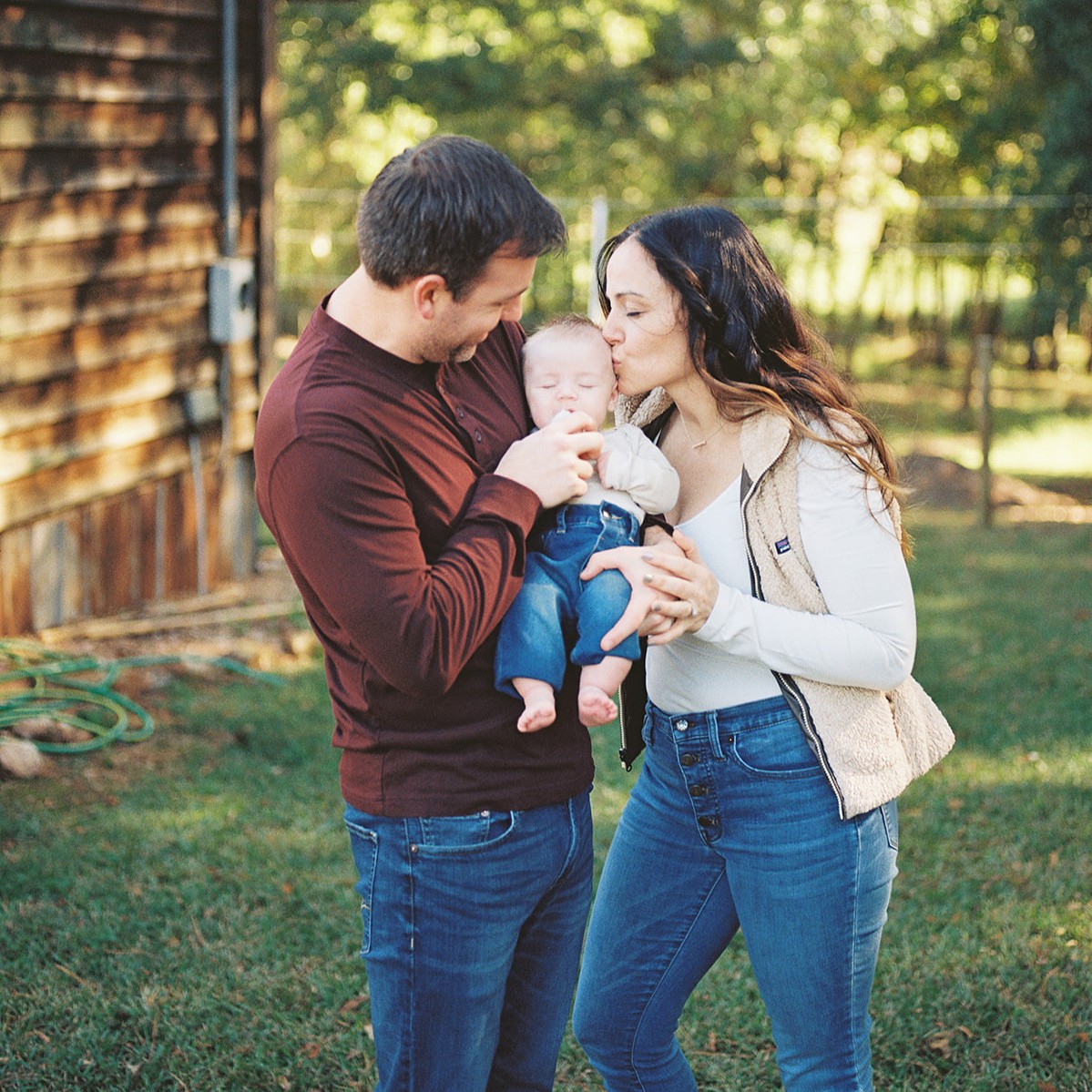 Fall family photo of a dad and mom kissing a newborn boy outside at Griffin's popular flower farm.