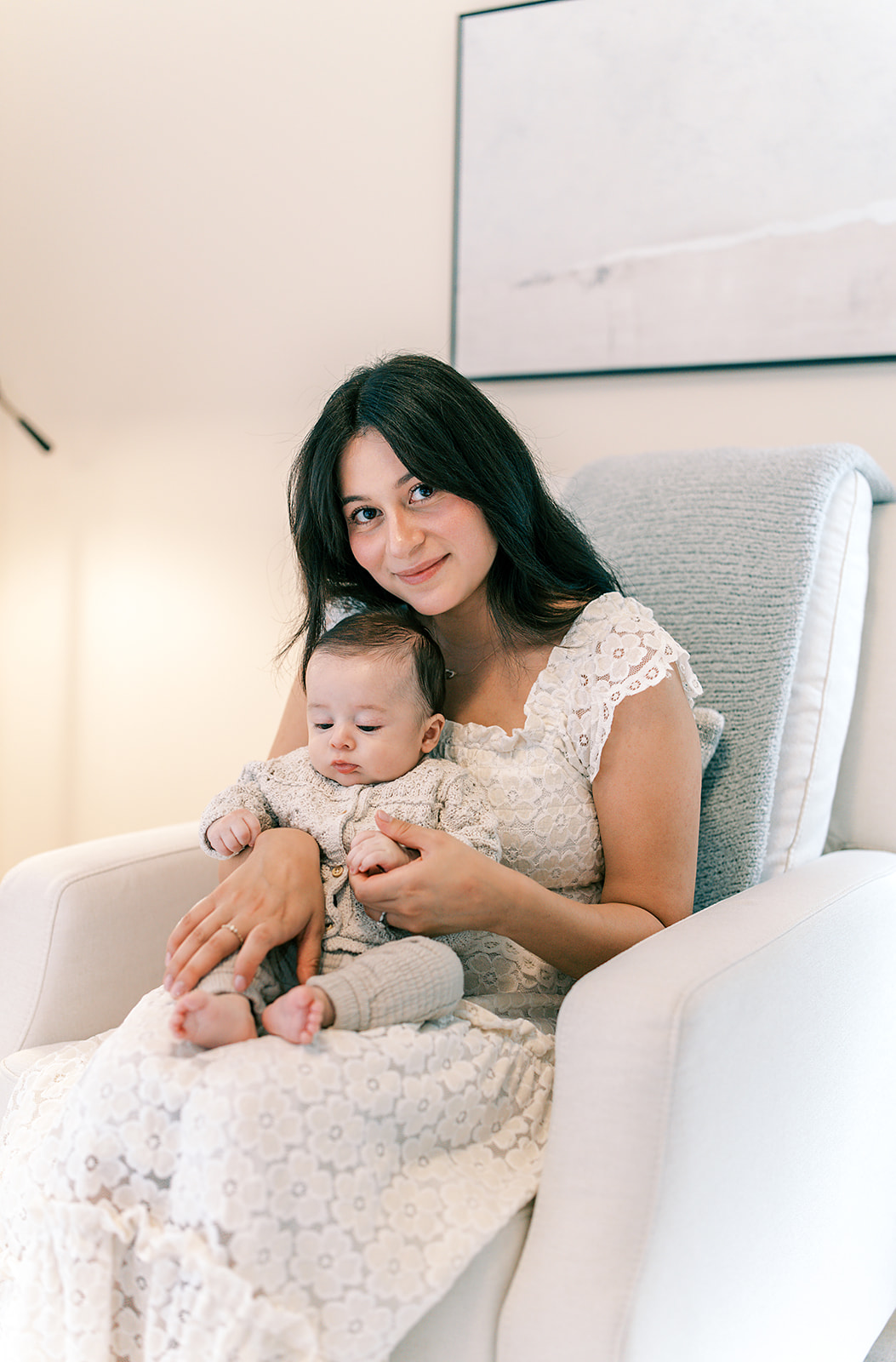 in home newborn session by holly ann co a senioa newborn photographer captures mom and baby boy on her lap inside his nursery glider chair